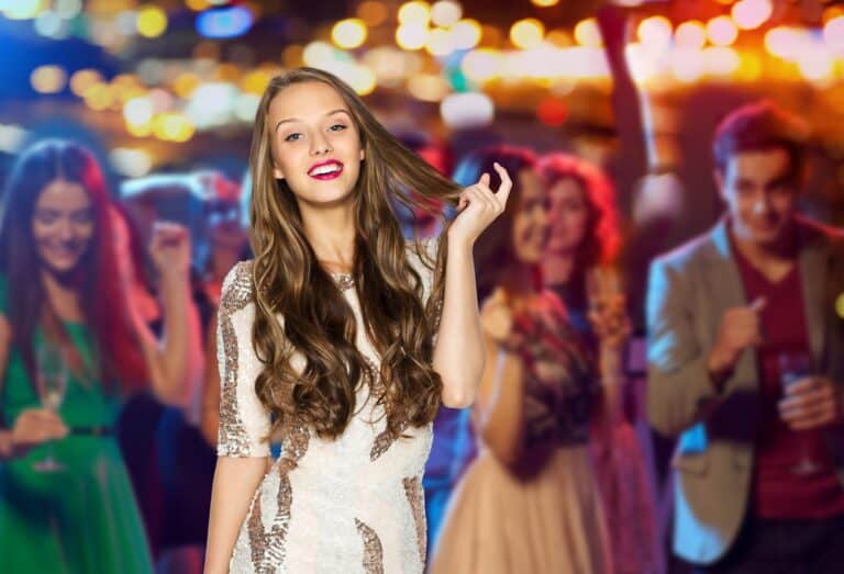 people, holidays, celebration and glamour concept - happy young woman or teen girl in fancy dress with sequins at night club party over crowd and lights background