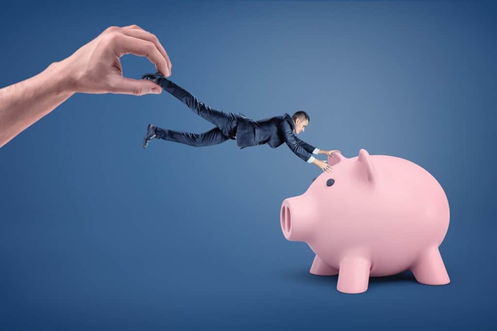 businessman-holding-onto-piggy-bank-while-being-pulled-away