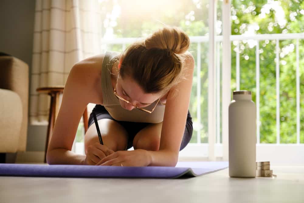 woman-writing-in-journal-while-sitting-on-yoga-matt