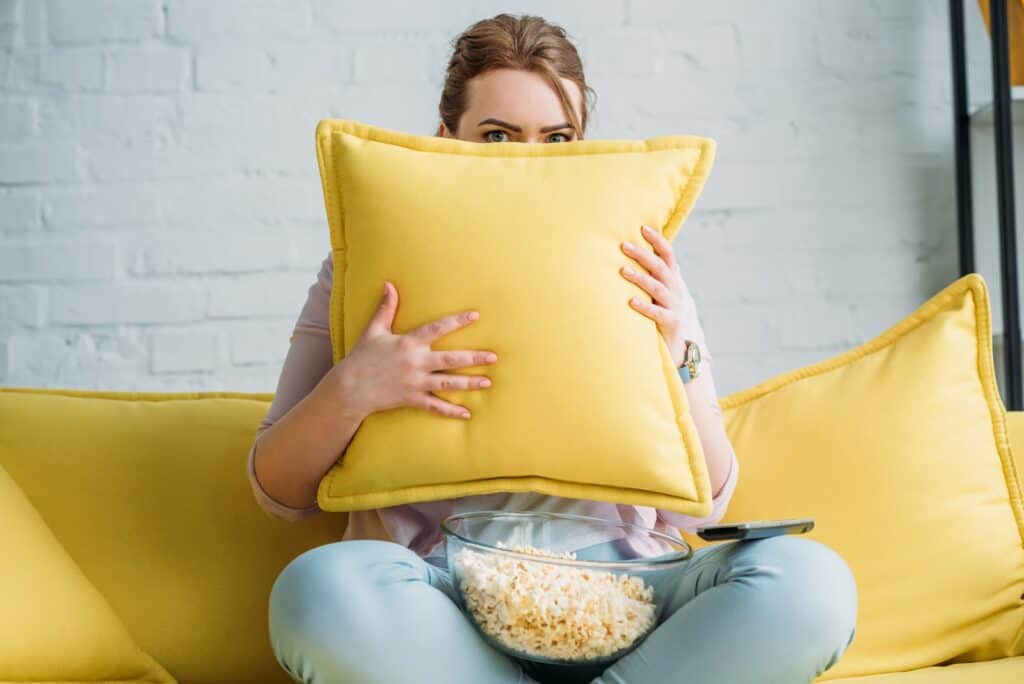 woman-sitting-on-couch-hiding-behind-pillow