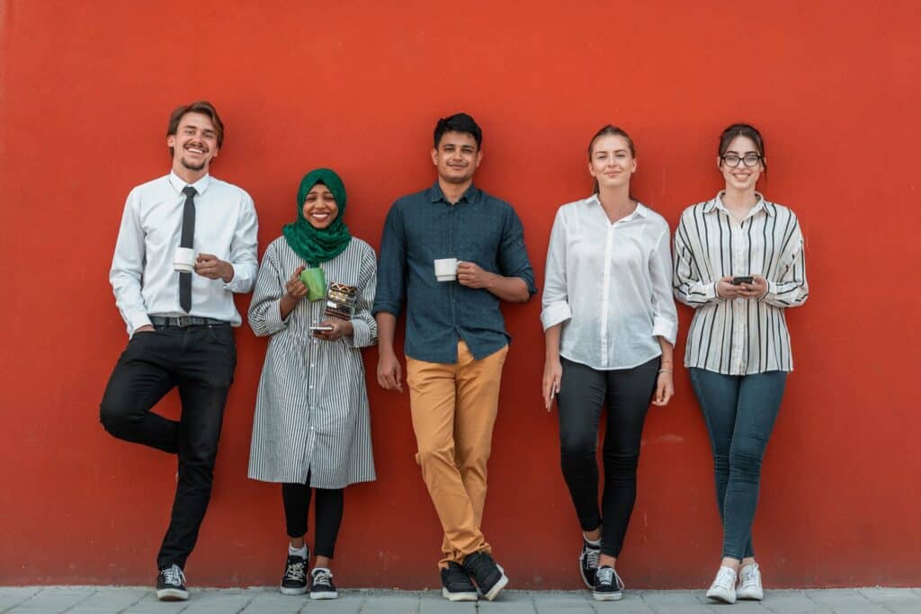 multiethnic-group-of-casual-businesspeople-using-smartphone-during-a-coffee-break-from-work-in-front-of-the-red-wall-outside