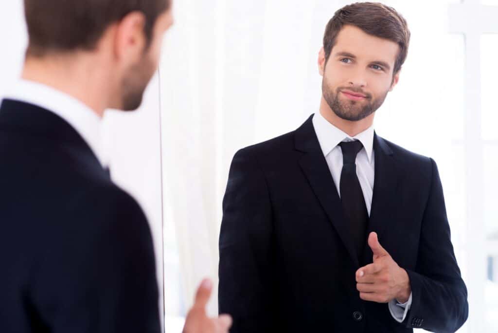 young-and-successful-handsome-young-man-in-full-suit-pointing-himself-and-smiling-while-standing-against-mirror