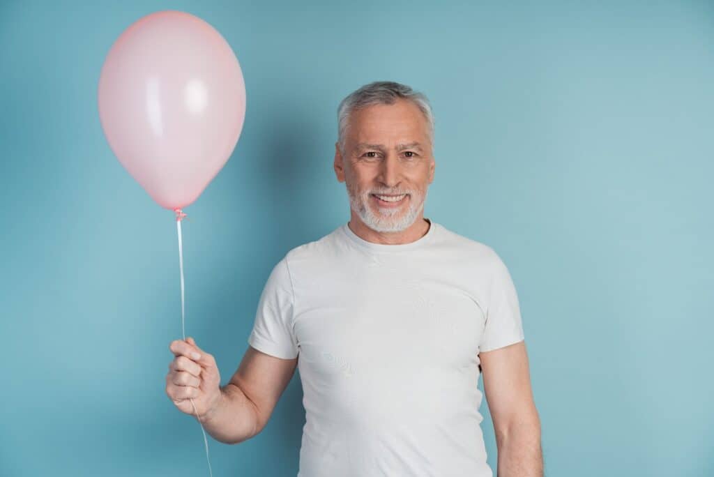 happy-retired-man-in-white-t-shirt-holding-pink-balloon
