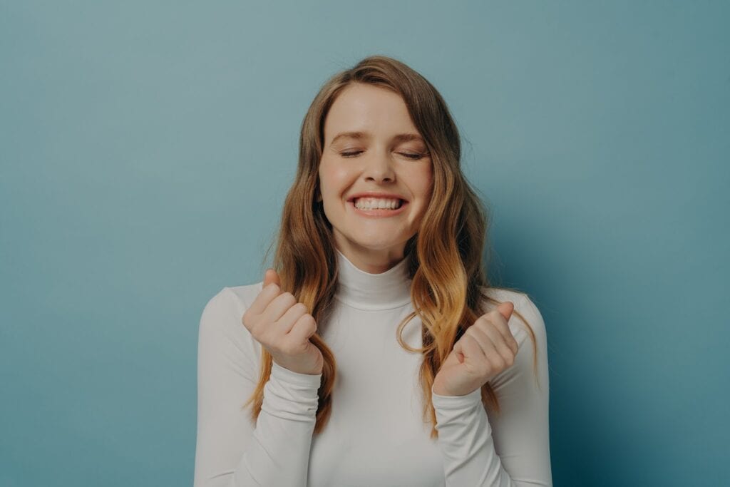 excited-young-lady-clenched-fists-waiting-for-miracle-with-eyes-closed-isolated-on-blue-background