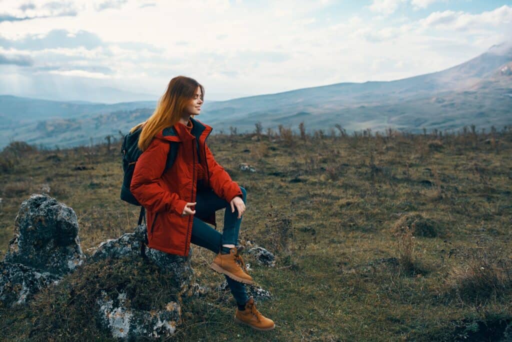 woman-traveler-in-a-jacket-sits-on-the-big-stone-and-looks-at-the-mountains-landscape