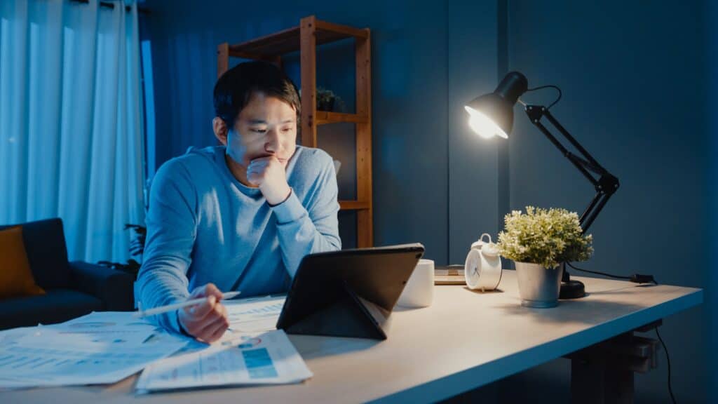 businessman-focus-work-pen-write-on-tablet-computer-busy-with-full-of-graph-paperwork-on-desk-in-living-room-at-home-overtime-at-night-work-from-home-during-covid-19-pandemic-concept