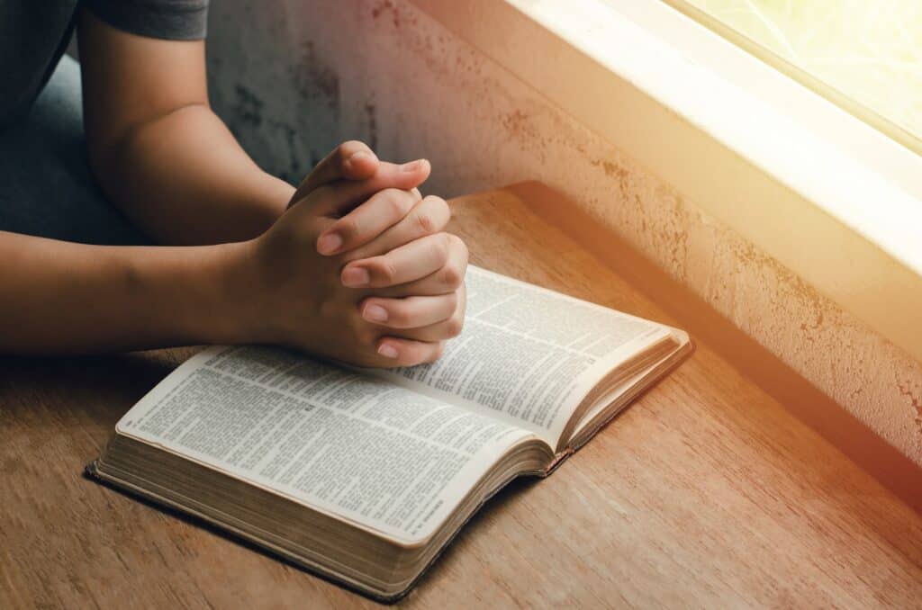 girl-sitting-and-praying-for-blessings-from-god-with-the-bible-folded-hands-in-biblical-spiritual-and-religious-prayer-communicate-talk-to-god-love-and-forgiveness