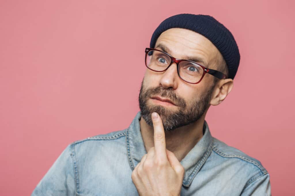 close up shot of thoughtful bearded male with blue eyes being deep in thoughts