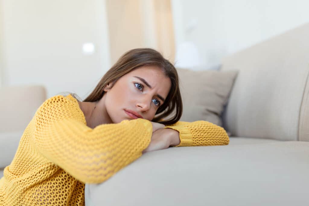 upset woman frustrated by problem with work or relationships sitting on couch covered face in hand feeling despair and anxiety