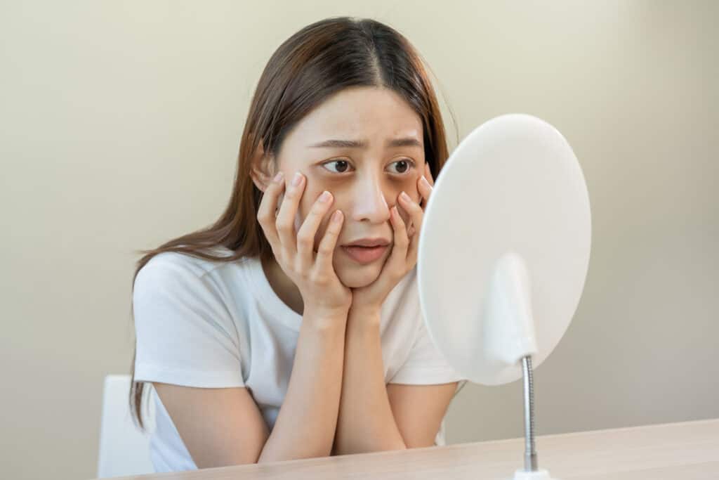 young woman girl looking at mirror hand touching under eyes and wrinkle on face sleepless