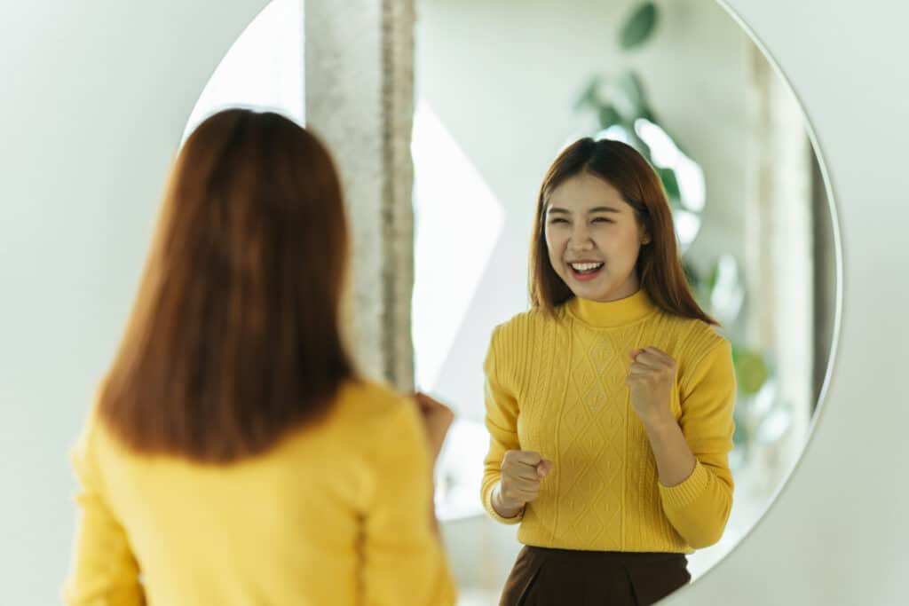 young woman talks to herself through a mirror to build her self confidence and empower herself