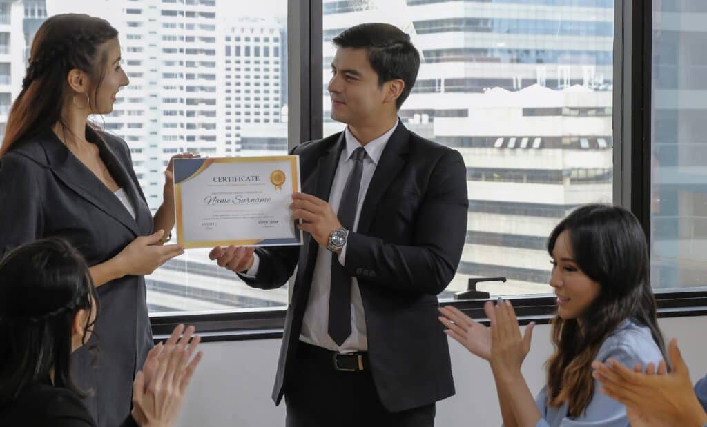 young-caucasian-manager-in-suit-giving-mock-up-certificate-to-woman-staff-with-happy-smiling-face-while-others-applauding-for-congratulation-in-office-meeting-room-selective-focus