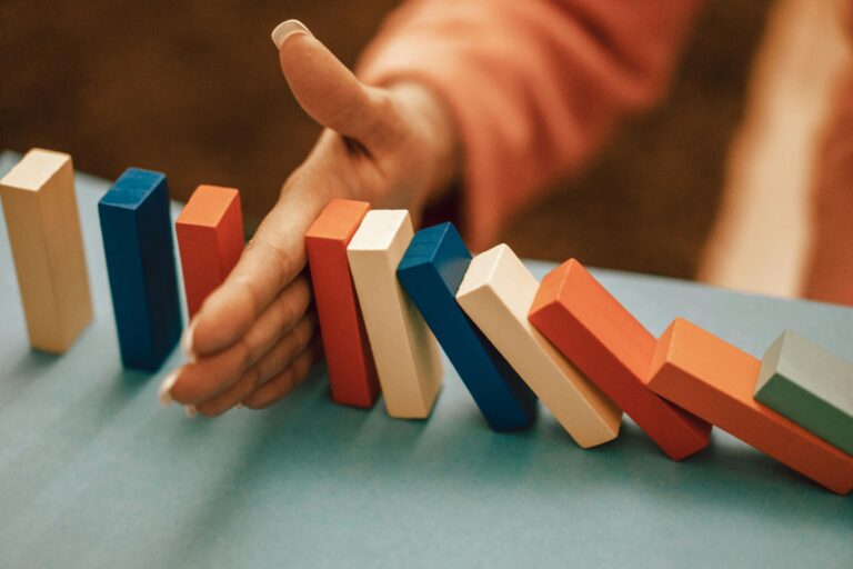 A hand strategically stops falling blue and red domino blocks on a table